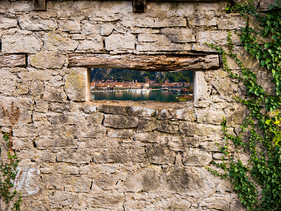 The old town of Kotor, Montenegro is seen through a window on an old, stone wall.